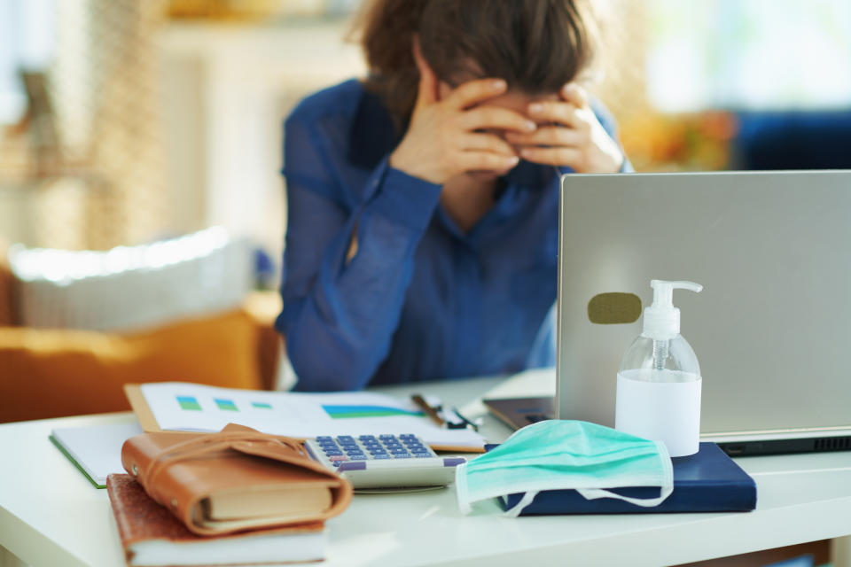 Closeup on medical mask and hand disinfectant and stressed woman in background in temporary home office during the coronavirus epidemic in the house in sunny day.