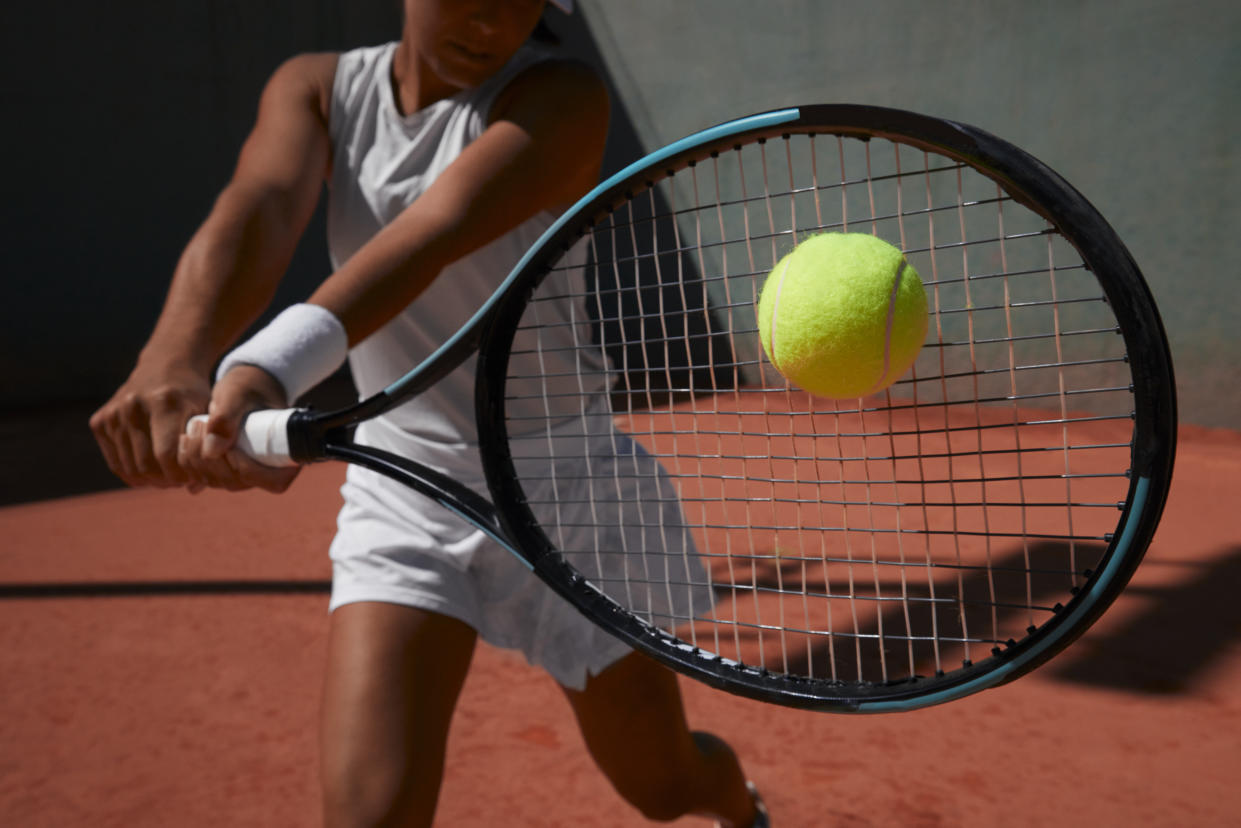 Tennis player appearing to strike tennis ball with racket.