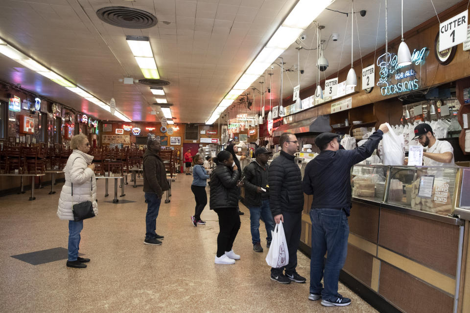 In this March 19, 2020 photo, customers wait for their to go orders at Katz's Delicatessen on the Lower East Side of New York. The iconic eatery is only open for take out and delivery orders due to the coronavirus outbreak. (AP Photo/Mary Altaffer)