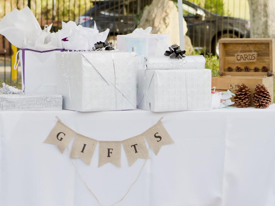 A table covered with a white tablecloth with a sign saying "Gifts" and wrapped presents