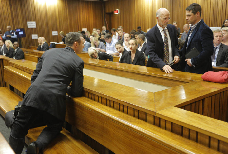 Oscar Pistorius, left, in the dock turns back to speak with his uncle, Arnold Pistorius, standing at left, and his brother Carl, standing at right, on the second day of his trial at the high court in Pretoria, South Africa, Tuesday, March 4, 2014. Pistorius is charged with murder for the shooting death of his girlfriend, Reeva Steenkamp, on Valentines Day in 2013. (AP Photo/Kim Ludbrook, Pool)