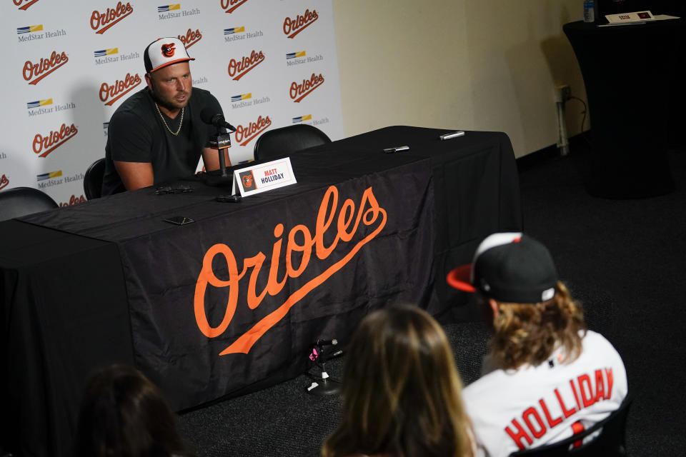 CORRECTS DATE - Jackson Holliday, bottom right, the first overall draft pick by the Baltimore Orioles in the 2022 draft, looks on as his father and former major league player Matt Holliday, top, speaks during a news conference introducing Jackson to the Baltimore media prior to a baseball game between the Baltimore Orioles and the Tampa Bay Rays, Wednesday, July 27, 2022, in Baltimore. (AP Photo/Julio Cortez)