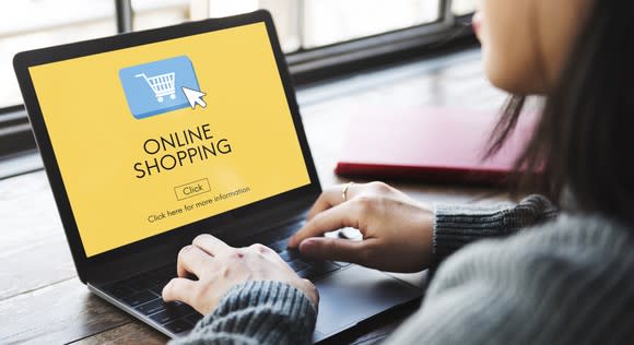 Woman sitting in front of a laptop computer with the words "online shopping" displayed.