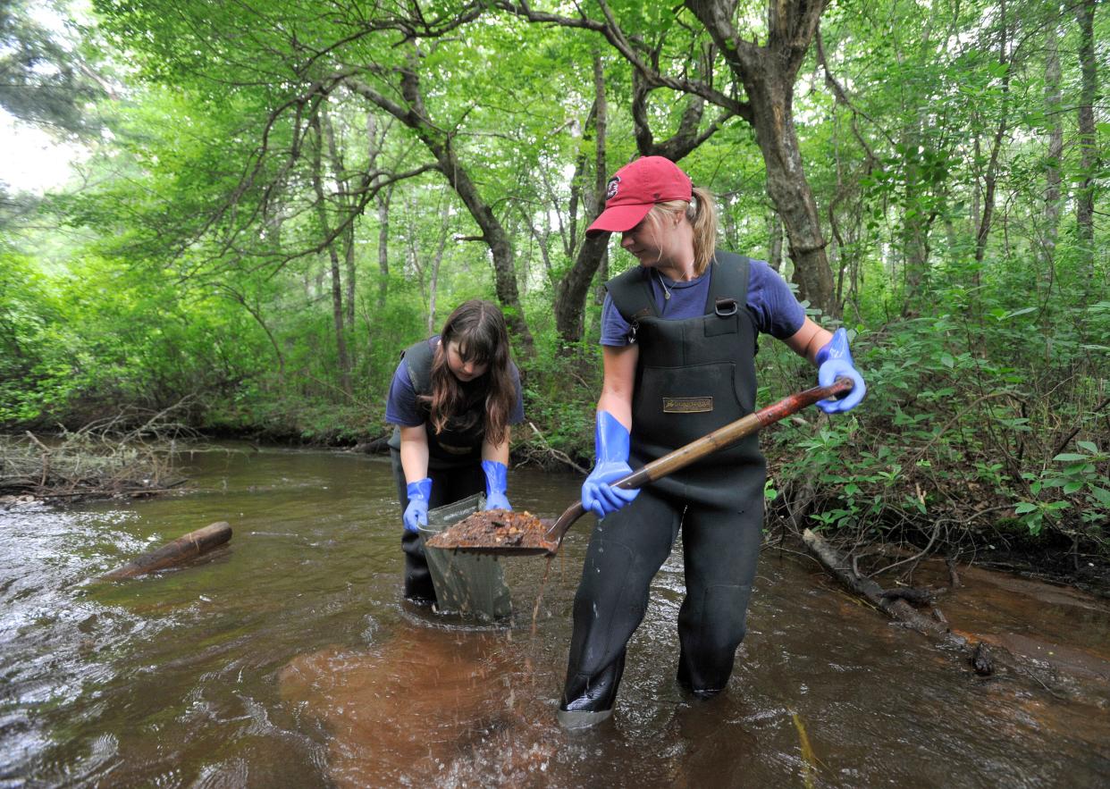 AmeriCorps Cape Cod members Grace Vachon, left, and Savannah Gray work together on July 11 in Mashpee to fill sand bags in the Quashnet River to be used for erosion control in another spot in the waterway. They were working with service partner Francis Smith of Trout Unlimited.