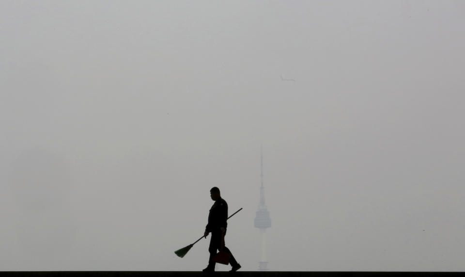 In this March 12, 2019, photo, a worker is silhouetted as the cityscape is covered with a thick haze of fine dust particles, at the National Museum of Korea in Seoul, South Korea. South Korean President Moon Jae-in on March 6, proposed a joint project with China to use artificial rain to clean the air in Seoul, where an acute increase in pollution has caused alarm. (AP Photo/Ahn Young-joon)