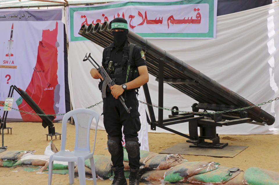 FILE - In this July 20, 2016 file photo, a masked Palestinian militant from the Izzedine al-Qassam Brigades, a military wing of Hamas, stands in front of rocket launchers during a weapon exhibition at a Hamas-run youth summer camp, in Gaza City. Over the years, the Islamic militant Hamas group has built up a large arsenal of rockets and missiles that have evolved from rudimentary short-range projectiles into powerful weapons capable of striking virtually anywhere in Israel. (AP Photo/Adel Hana, File)