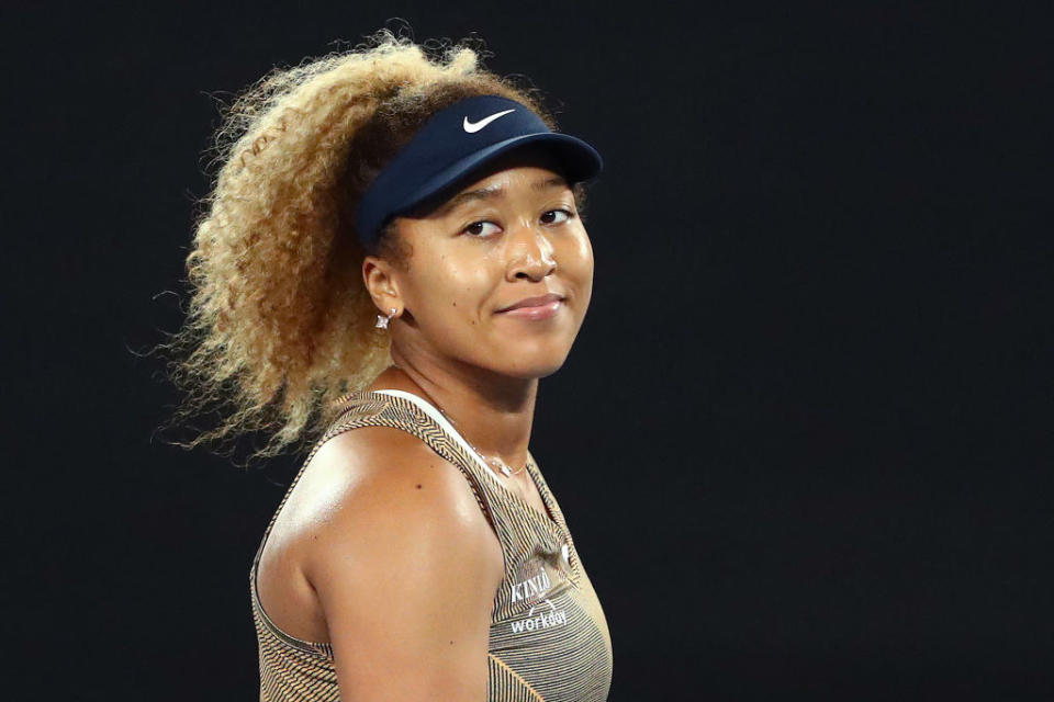 Naomi smiles while standing on a tennis court