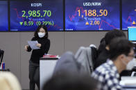 A currency trader passes by screens showing the Korea Composite Stock Price Index (KOSPI) and the foreign exchange rate between U.S. dollar and South Korean won, right, at the foreign exchange dealing room of the KEB Hana Bank headquarters in Seoul, South Korea, Thursday, Nov. 25, 2021. Asian stock markets fell Thursday after Federal Reserve officials indicated they were ready to raise interest rates sooner than expected if needed to cool inflation.(AP Photo/Ahn Young-joon)