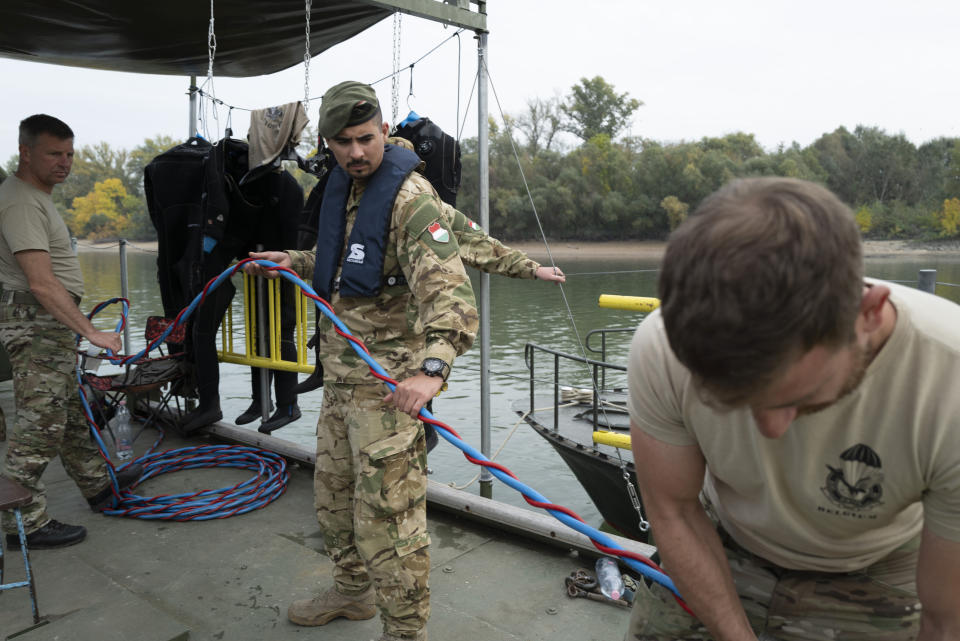 Belgian and Hungarian supporting soldiers adjust an oxygen pipe to a military diver on the Danube River in Budapest, Hungary, Friday, Oct. 13, 2023, during an international training exercise which prepares military divers to find and remove unexploded underwater ordnances. Hungary this year hosted the 10-day exercise for the second year in a row and provided the soldiers from Hungary, Germany, Belgium and Lithuania with hands-on training in a variety of environments, like facing the powerful current of the Danube River. (AP Photo/Bela Szandelszky)