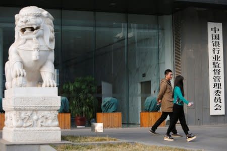 People walk past a sign of China Banking Regulatory Commission (CBRC) at its office in Beijing, China March 13, 2018.  REUTERS/Florence Lo