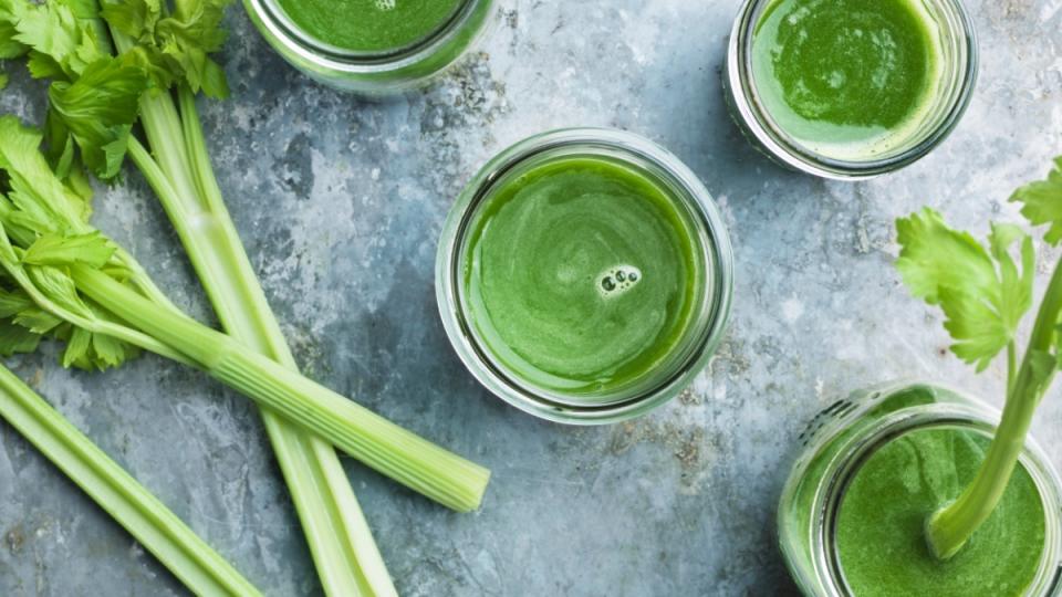 Glasses of celery juice, a drink that lowers blood pressure quickly, on a slate table beside fresh celery