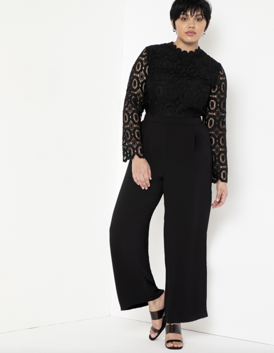 short hair model posing in long sleeve black lace jumpsuit and heels