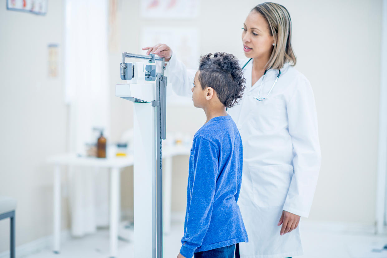 Doctor taking a teenager's measurements while he stands on a scale