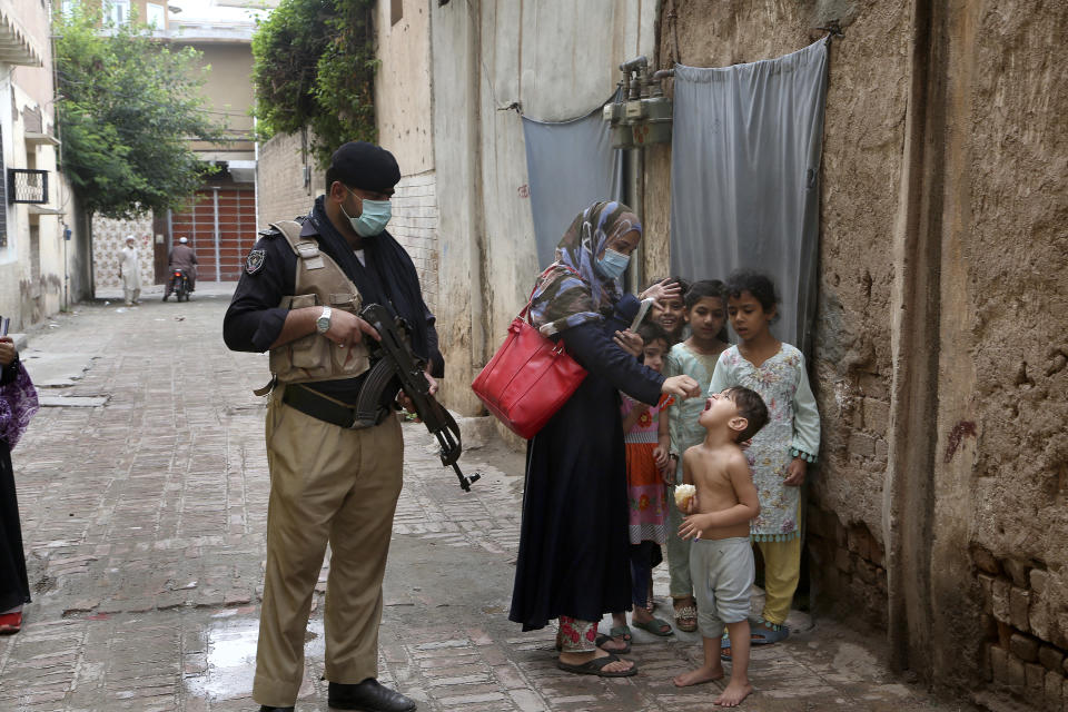A police officer stand guard while a healthcare worker administers a polio vaccine to a child in Peshawar, Pakistan, Friday, July 30, 2021. The Pakistani government launched an anti-polio vaccination campaign in an effort to eradicate the crippling disease. (AP Photo/Muhammad Sajjad)