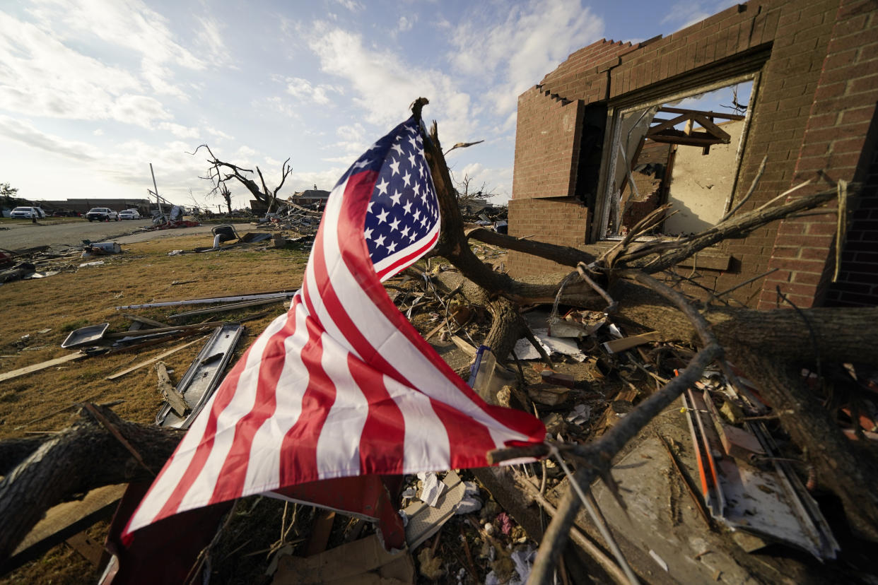 FILE - An American flag flies amidst debris of destroyed homes, in the aftermath of tornadoes that tore through the region, in Mayfield, Ky., Tuesday, Dec. 14, 2021. According to three different reports released Monday, Jan. 10, 2021, the United States staggered through a steady onslaught of deadly billion-dollar climate disasters in an extra hot 2021, while the nation’s greenhouse gas emissions last year jumped 6% because of surges in coal and long-haul trucking, putting America further behind its 2030 climate change cutting goal. (AP Photo/Gerald Herbert, File)