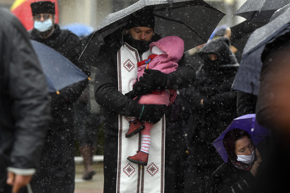 A priest holds a baby during a religious service celebrating St. Andrew in the village of Ion Corvin, eastern Romania, Monday, Nov. 30, 2020. Braving wintry weather and the new coronavirus fears, several hundred Orthodox Christian believers gathered outside a cave in eastern Romania where St. Andrew is said to have lived and preached in the 1st century. (AP Photo/Andreea Alexandru)