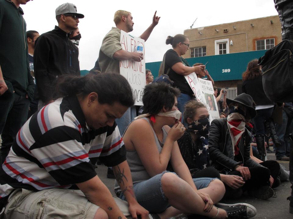 Protesters sit in downtown Albuquerque, N.M. during a rally Sunday March 30, 2014, against recent police shootings. Hundreds of protesters marched past riot police in Albuquerque on Sunday, days after a YouTube video emerged threatening retaliation for a recent deadly police shooting. The video, which bore the logo of the computer hacking collective Anonymous, warned of a cyber attack on city websites and called for the protest march. (AP Photo/Russell Contreras)