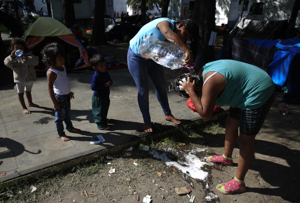 Women use water from a bottle to wash their hair in a sports complex where thousands of migrants have been camped out for several days in Mexico City, Friday, Nov. 9, 2018. About 500 Central American migrants headed out of Mexico City on Friday to embark on the longest and most dangerous leg of their journey to the U.S. border, while thousands more were waiting one day more at a massive improvised shelter.(AP Photo/Rebecca Blackwell)