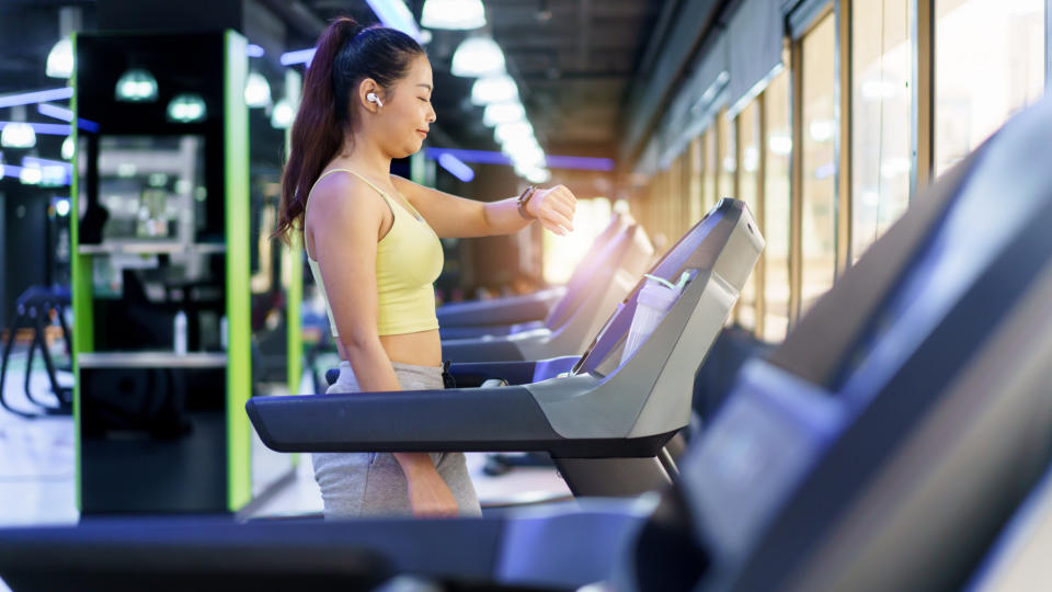 Woman walking on a treadmill in a gym, looking at her fitness tracker on her wrist