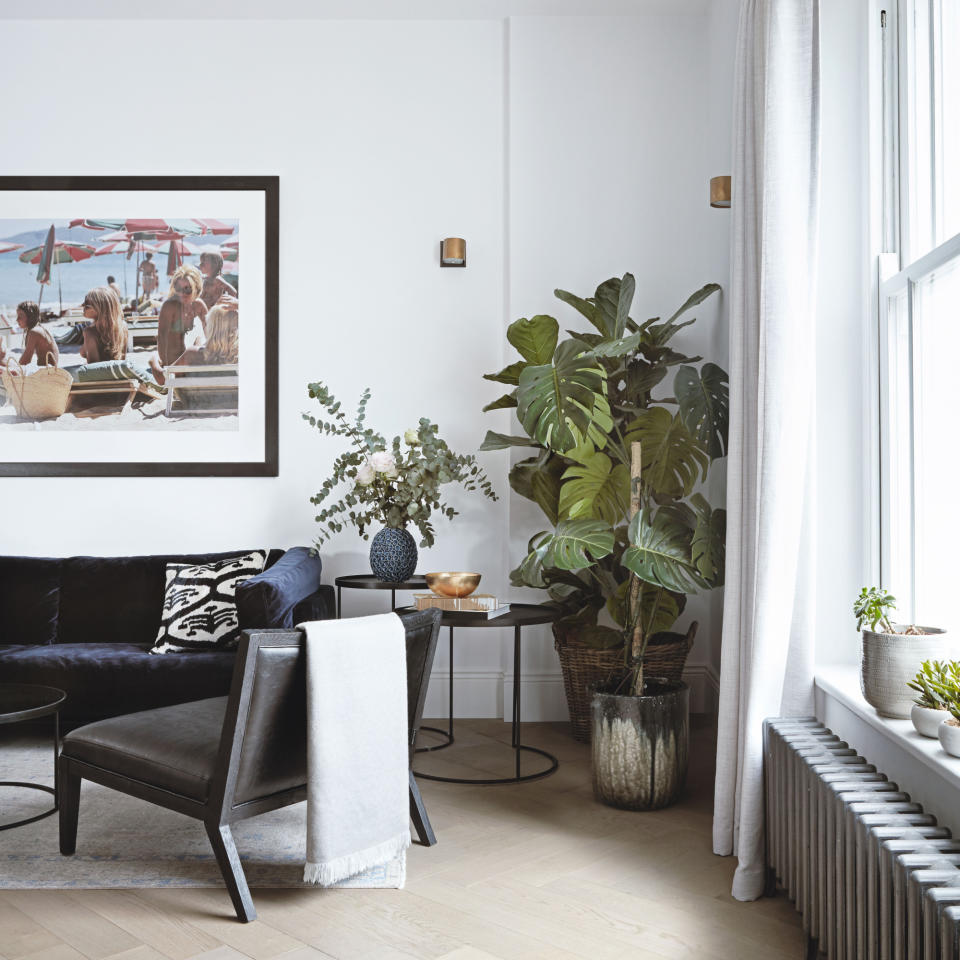 Living room with white walls, wooden floor and metal radiator below a sash window with white curtains