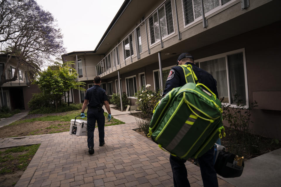 Torrance firefighters Trevor Borello, left, and Alessandro Demuro carry a cooler containing the Pfizer COVID-19 vaccine and medical equipment as they walk to an apartment to inoculate two sisters who have muscular dystrophy, Wednesday, May 12, 2021, in Torrance, Calif. Teamed up with the Torrance Fire Department, Torrance Memorial Medical Center started inoculating people at home in March, identifying people through a city hotline, county health department, senior centers and doctor's offices, said Mei Tsai, the pharmacist who coordinates the program. (AP Photo/Jae C. Hong)