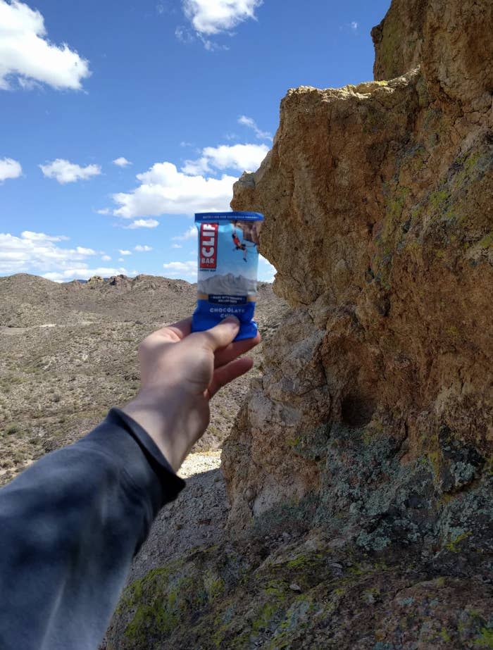 Person's hand holding a Clif energy bar with rocky terrain in the background