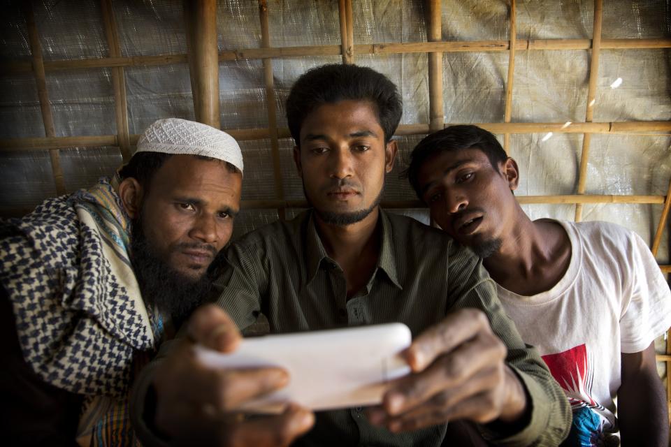 FILE – In this Jan. 14, 2018, file photo, Rohingya Muslim refugees look at a cellphone at the Kutupalong refugee camp, in Bangladesh. Internal company documents from the former Facebook product manager-turned-whistleblower Frances Haugen show that in some of the world's most volatile regions, terrorist content and hate speech proliferate because the company remains short on moderators who speak local languages and understand cultural contexts. (AP Photo/Manish Swarup, File)