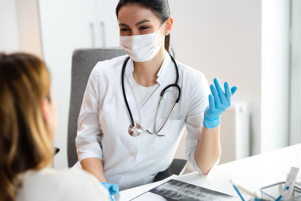 Caucasian doctor in medical mask speaking with mother about scoliosis of her daughter stock photo. Pediatrics concept