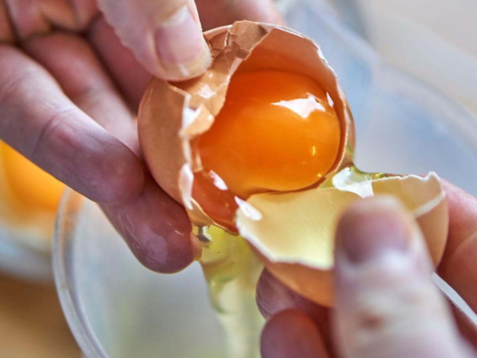 a close up of an egg yolk in the shell, with a pair of hands separating out the egg white