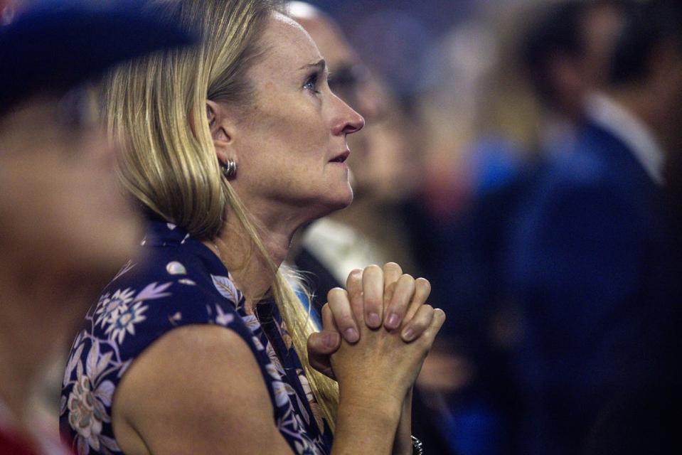 photograph of a woman praying while looking at Donald Trump at the Republican National Convention 2024