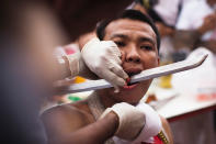 PHUKET, THAILAND - OCTOBER 05: A devotee of the Chinese shrine of Sui Boon Tong Shrine, pierces his cheeks with a sword during a procession at the Vegetarian Festival on October 5, 2011 in Phuket, Thailand. Ritual Vegetarianism in Phuket Island traces it roots back to the early 1800's. The festival begins on the first evening of the ninth lunar month and lasts for nine days. Participants in the festival perform acts of body piercing as a means of shifting evil spirits from individuals onto themselves and bring the community good luck. (Photo by Athit Perawongmetha/Getty Images)