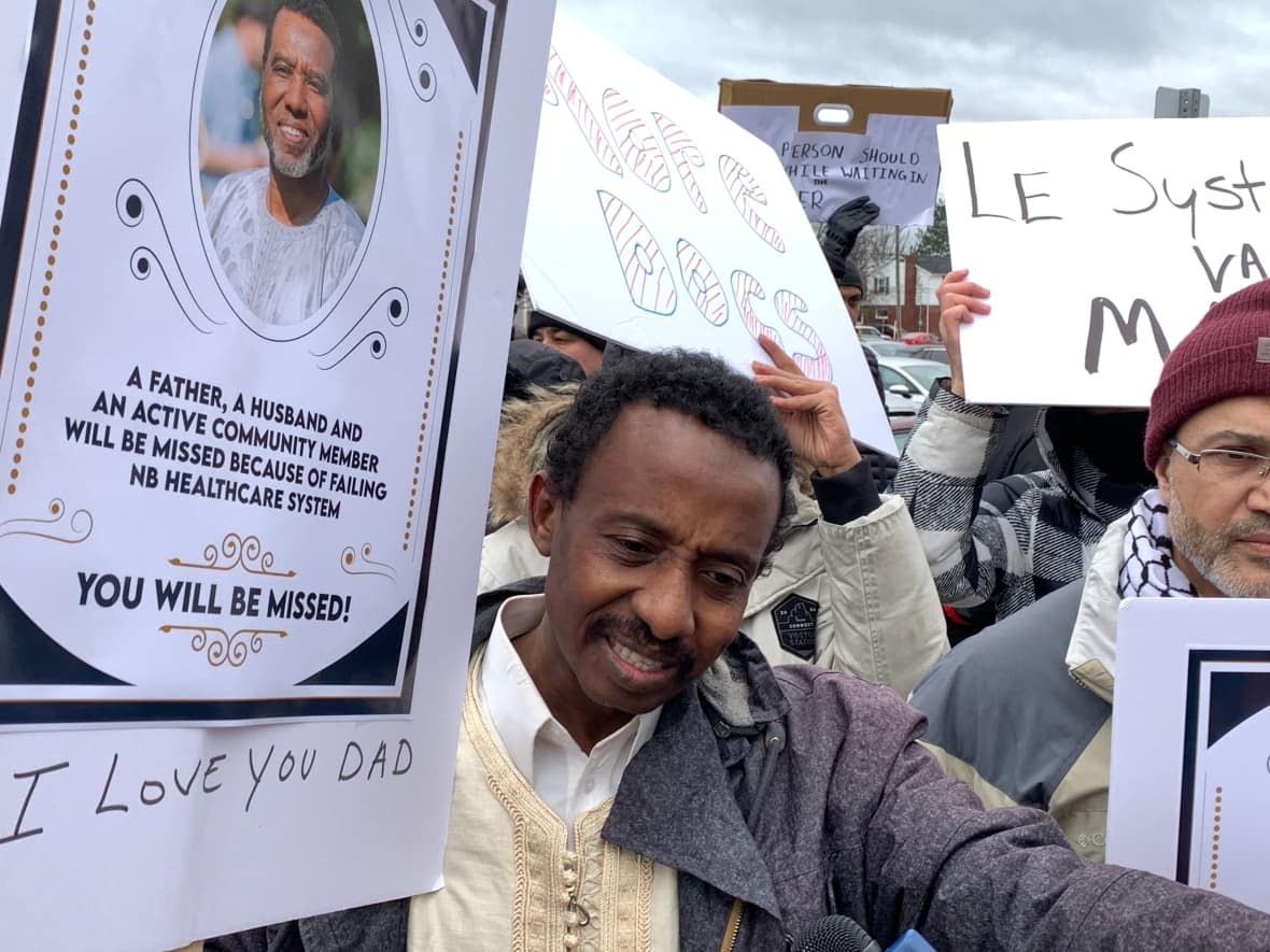 A protester holds a sign with a picture of a Moncton man, only identified as MS, who died at the Moncton Hospital waiting room last Wednesday. (Pascal Raiche-Nogue/Radio Canada - image credit)