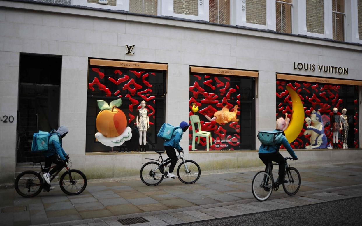 Cyclists delivering takeaway meals ride past closed shop windows in Mayfair, London W1, as lockdown continues - Tolga Akmen/AFP