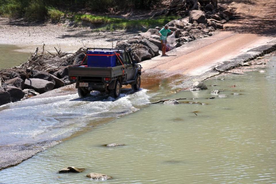 A car passing a fisherman preparing to cast his net at Cahills Crossing on the East Alligator River in the world heritage site of Kakadu National Park.