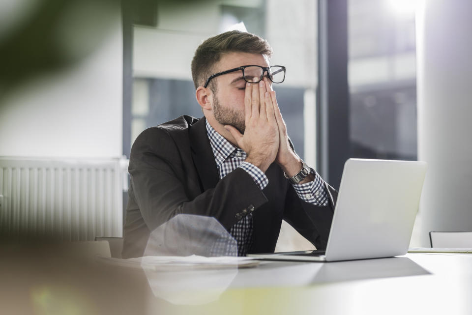 A man rubbing his eyes in front of his computer