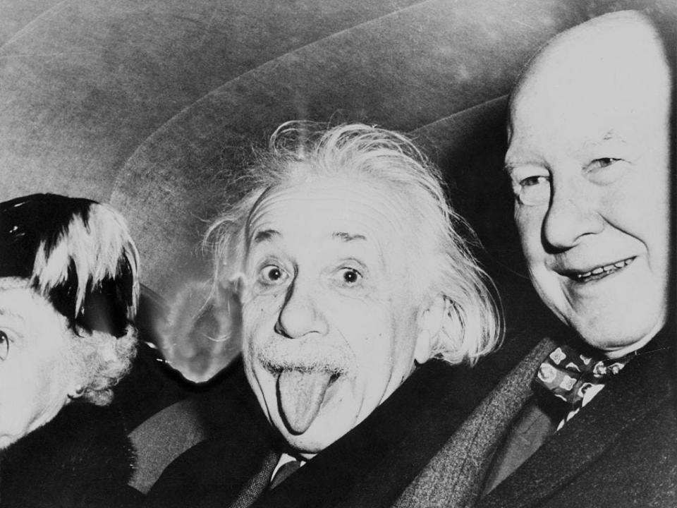 Einstein sticks his tongue out standing next to another man