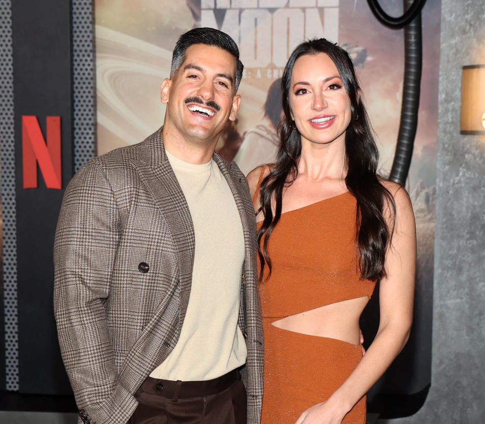 Alexandra Madison and Jon Bouffard pose on a red carpet. Bouffard in a brown plaid jacket and Madison in a rust orange dress. (Phillip Faraone / Getty Images for Netflix)