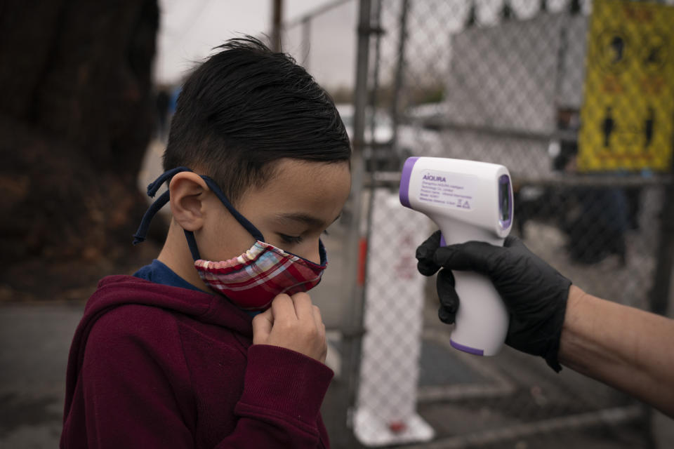 Adam Alvarado, 6, gets his temperature checked on the first day of in-person learning at Heliotrope Avenue Elementary School in Maywood, Calif., Tuesday, April 13, 2021. More than a year after the pandemic forced all of California's schools to close classroom doors, some of the state's largest school districts are slowly beginning to reopen this week for in-person instruction. (AP Photo/Jae C. Hong)