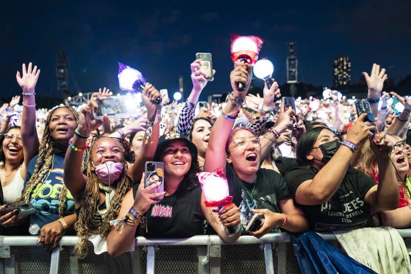 A crowd of concertgoers are reaching their hands out and filming with their phones, many with mouths open and smiling