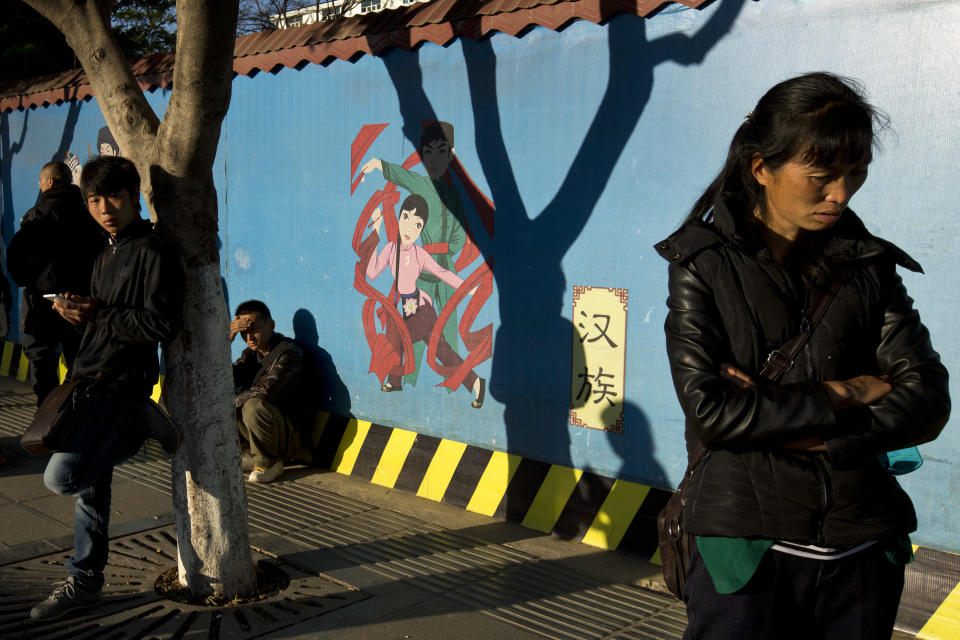 In this Monday, March 3, 2014 photo, people stand on a street near a wall painted with figures representing Han Chinese, center, and other ethnic groups living in the city as part of a tourism advertisement outside the Kunming Train Station in Kunming, in western China's Yunnan province. China said the vicious slashing spree Saturday that killed 29 people in the southern city was the work of separatists linked to international terrorism, but the assailants’ homespun methods and low-tech weapons - nothing more than long knives - have led some analysts to suspect they didn’t get outside help. (AP Photo/Alexander F. Yuan)