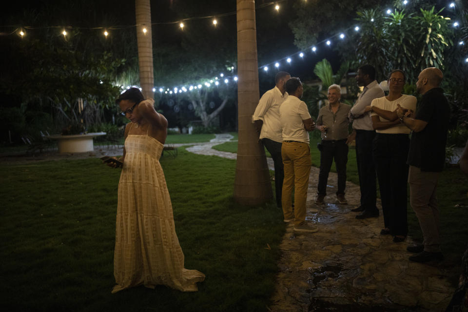 Businesswoman Magalie Dresse steps away to her view her cellphone messages during a garden cocktail party at her home in Port-au-Prince, Haiti, Wednesday, Sept. 15, 2021. During the party for friends and associates, they swapped stories about the impossibility of business life in a gangster nation. (AP Photo/Rodrigo Abd)