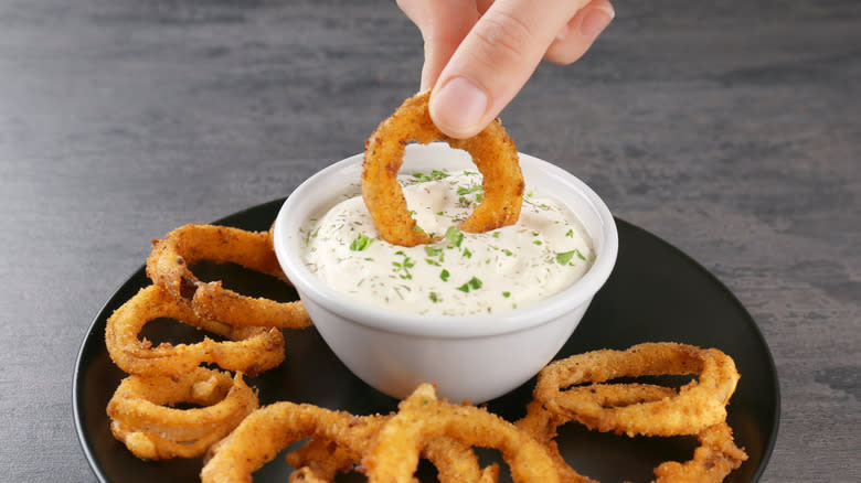 hand dipping an onion ring in sauce