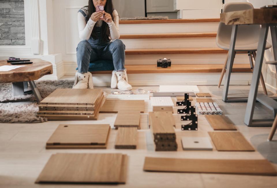 woman using phone while putting together furniture at home DIY