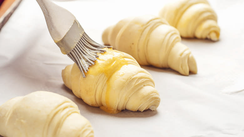 Egg wash being brushed on croissants