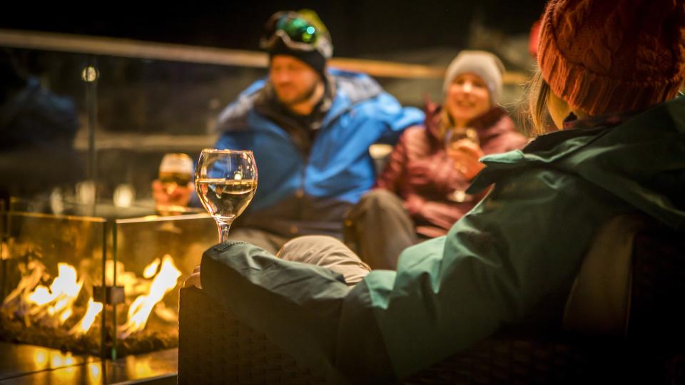 Friends enjoying drinks by fire at outdoor patio in a pub