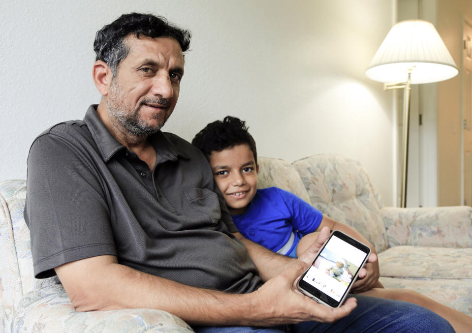 In this Sept. 29, 2018 photo, Hadi Mohammed sits with his 9 year old son Mohammed Ghaleb, as he displays a photo of his son as a baby in Baghdad, in their Lincoln, Neb. apartment. Death threats drove Hadi Mohammed out of Iraq and to a small apartment in Nebraska, where he and his two young sons managed to settle as refugees. But the danger hasn’t been enough to allow his wife to join them. (AP Photo/Nati Harnik)