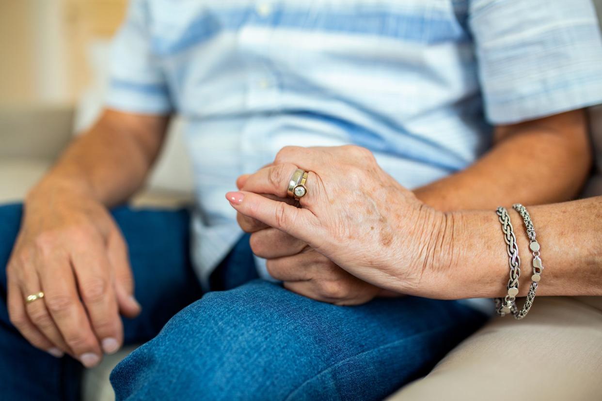 Close up of mature old husband and wife hold hands show love and care. Senior couple holding hands while sitting together at home. Elderly relationships, marriage concept