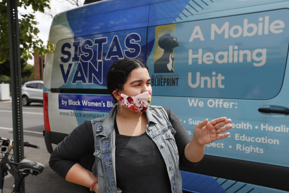 Sistas Van driver Denise Rodriguez pauses in front of the van she uses to pick up and drop off supplies for those in need of help amid the coronavirus outbreak, Tuesday, May 19, 2020, in New York. Originally launched to help survivors of sexual and reproductive violence and physical abuse, the women's network and their van have been delivering badly-needed resources to black and Hispanic communities, which have been disproportionately affected by the fast-spreading virus. (AP Photo/Kathy Willens)