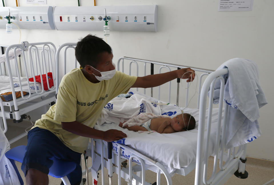 A Yanomami adjusts tubing near a baby who is receiving medical treatment, at the Santo Antonio Children's Hospital, in Boa Vista, Roraima state, Brazil, Thursday, Jan 26, 2023. Brazil's government declared a public health emergency for the Yanomami people in the Amazon, who are suffering from malnutrition and diseases such as malaria. (AP Photo/Edmar Barros)