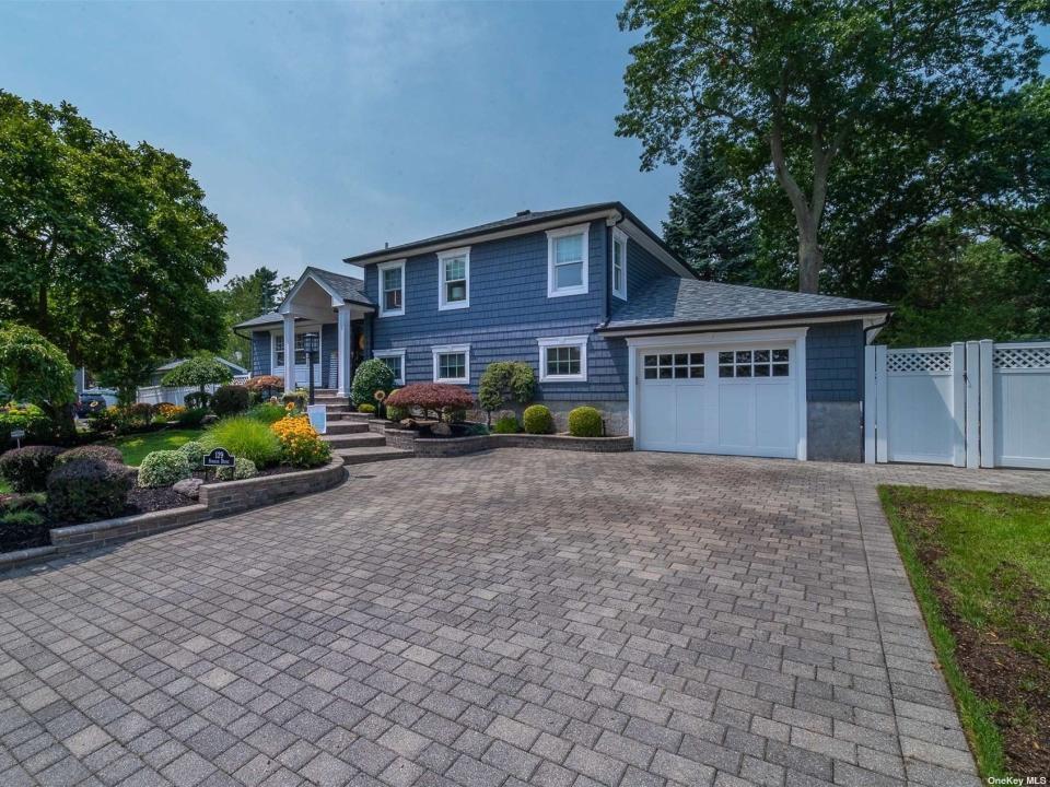 The blue exterior of the house for sale in Long Island with driveway in the foreground and garage door in the background